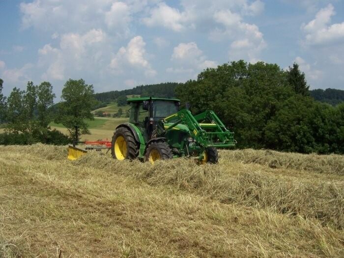 Ein Traktor steht auf einer gemähten Wiese zwischen dem Heu.